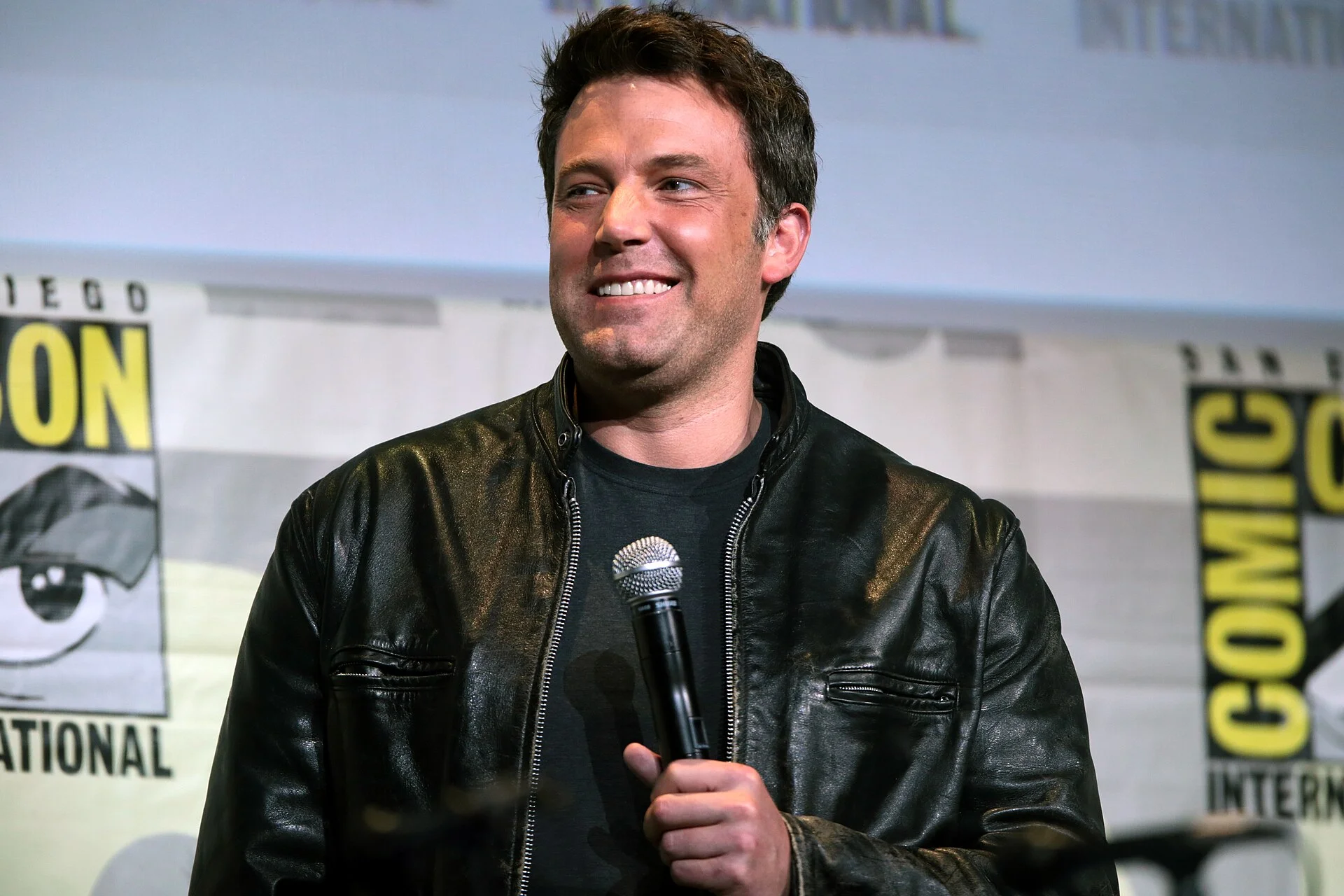 Ben Affleck photographed smiling on a convention panel stage in July 2016. Licensed image; it identifies the person only and is not evidence of any dental treatment.